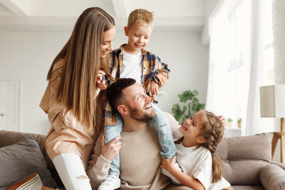 BODYMIND CAMPUS: Seminare für mehr Work-Life-Balance Eine glückliche, junge, vierköpfige Familie sitzt lachend und spielend auf der Couch.